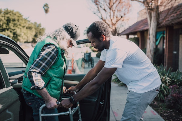 Un jeune homme aidant un vieil homme à sortir du véhicule